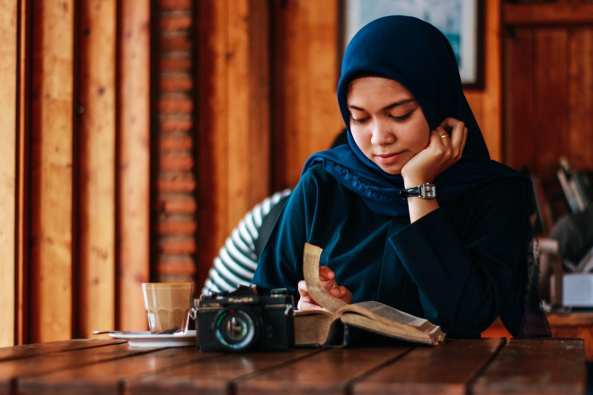 girl sitting next to a wooden table and reading a book