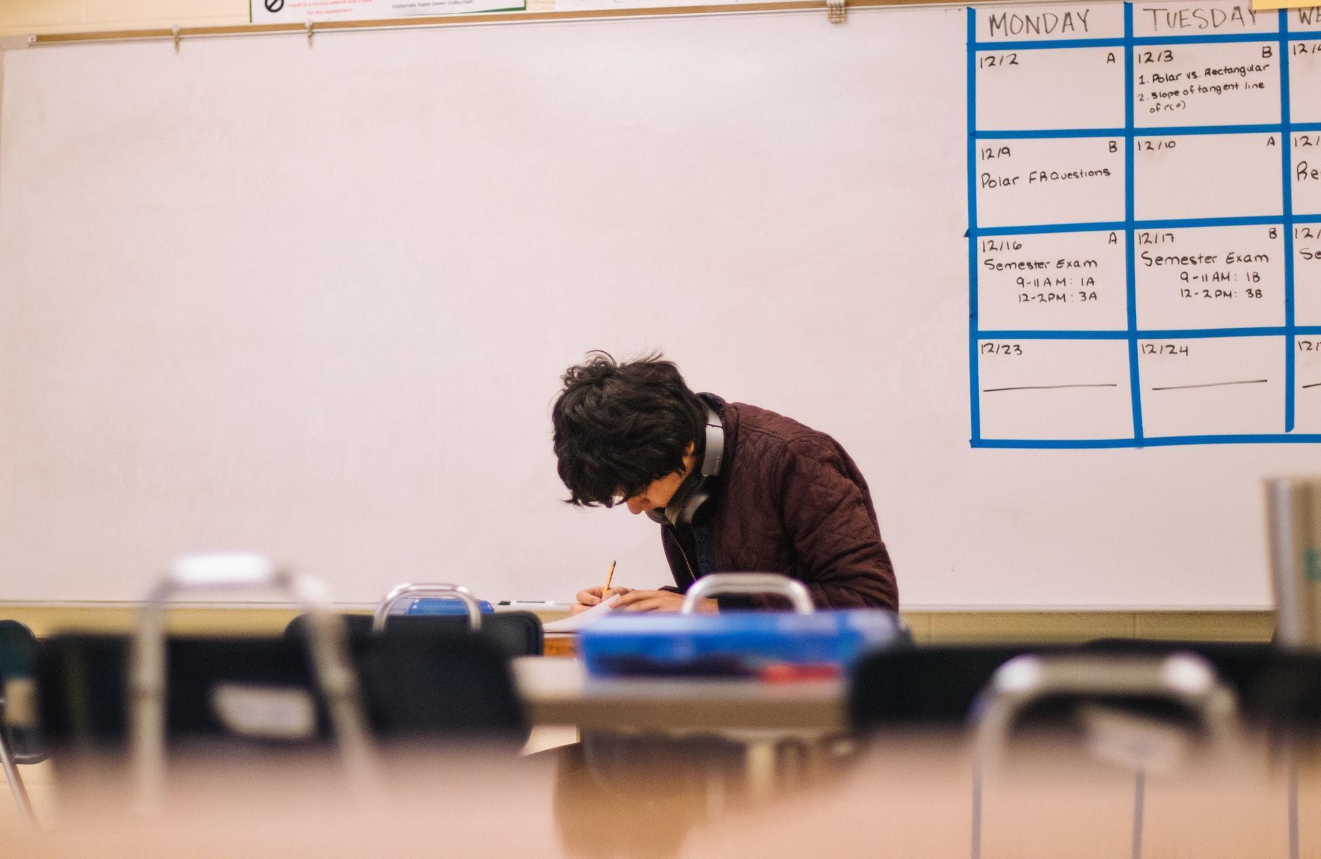 A young man sitting next to a table staring down holding a pencil