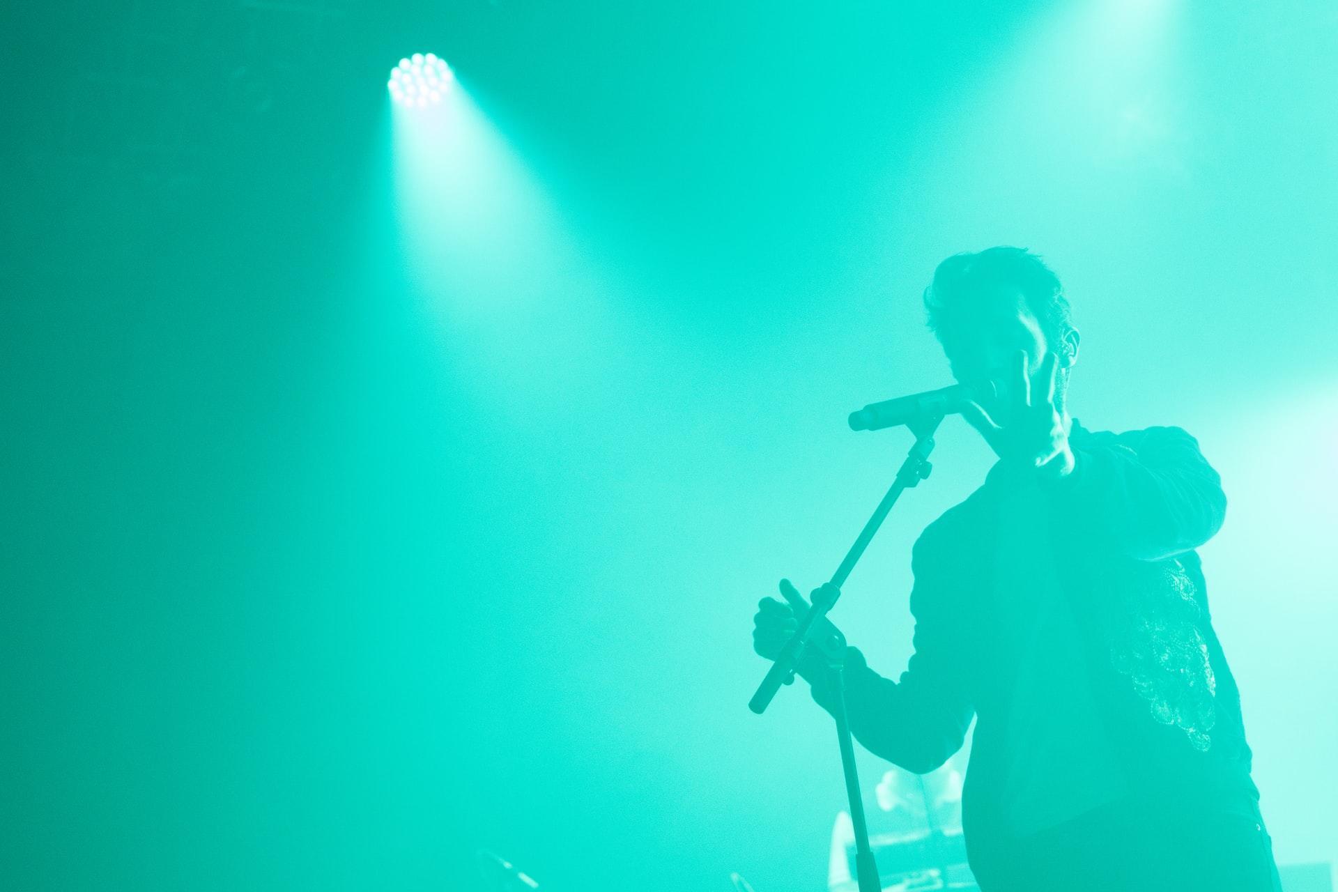 man singing next to microphone in front of blue lighting