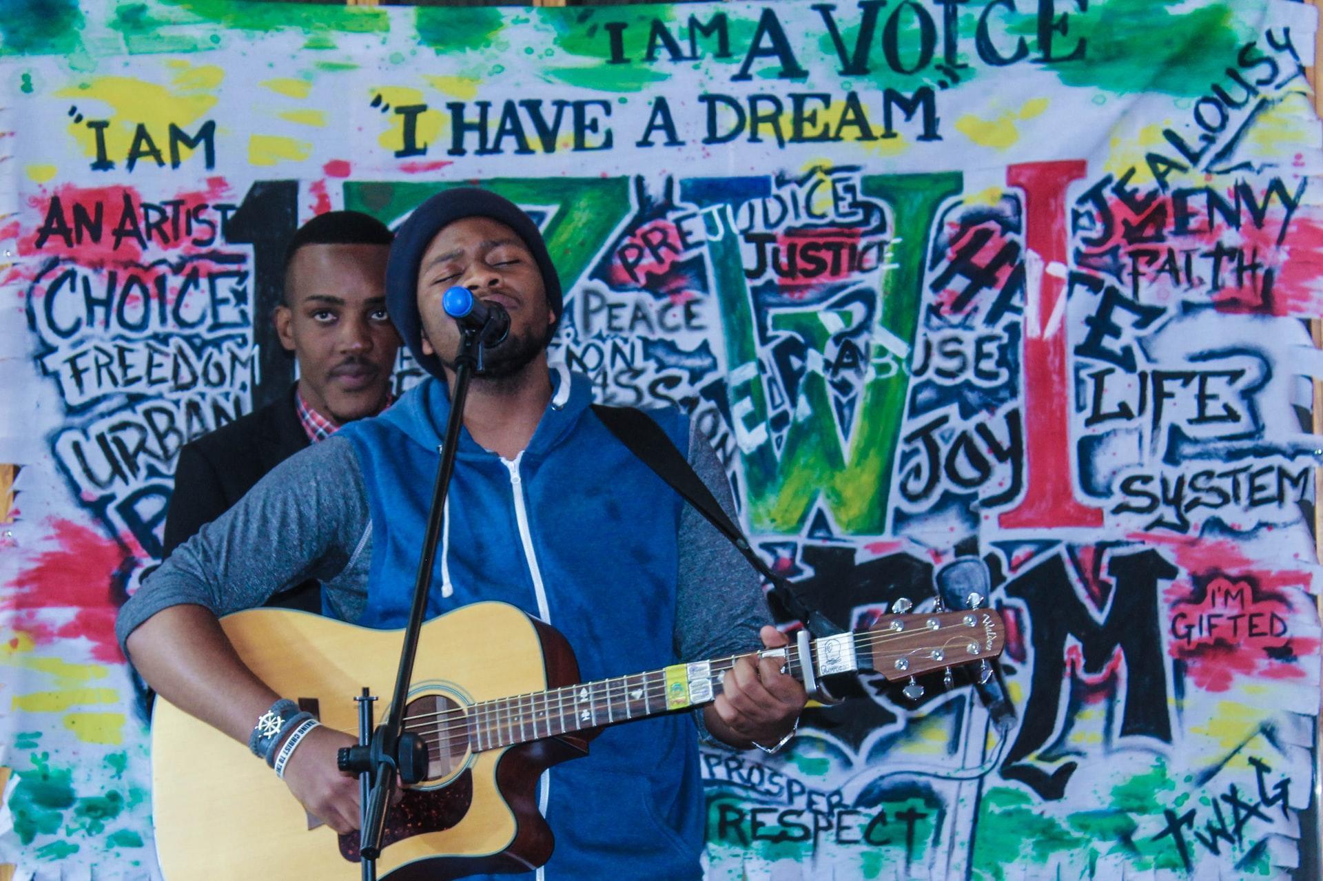 Man holding guitar and singing along in front of a gratified wall.