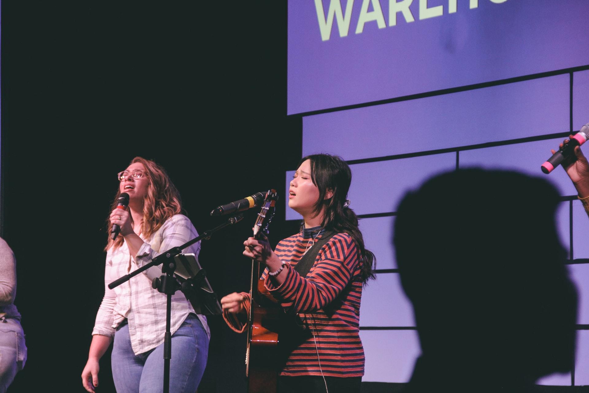 Two ladies singing together next to a microphone.
