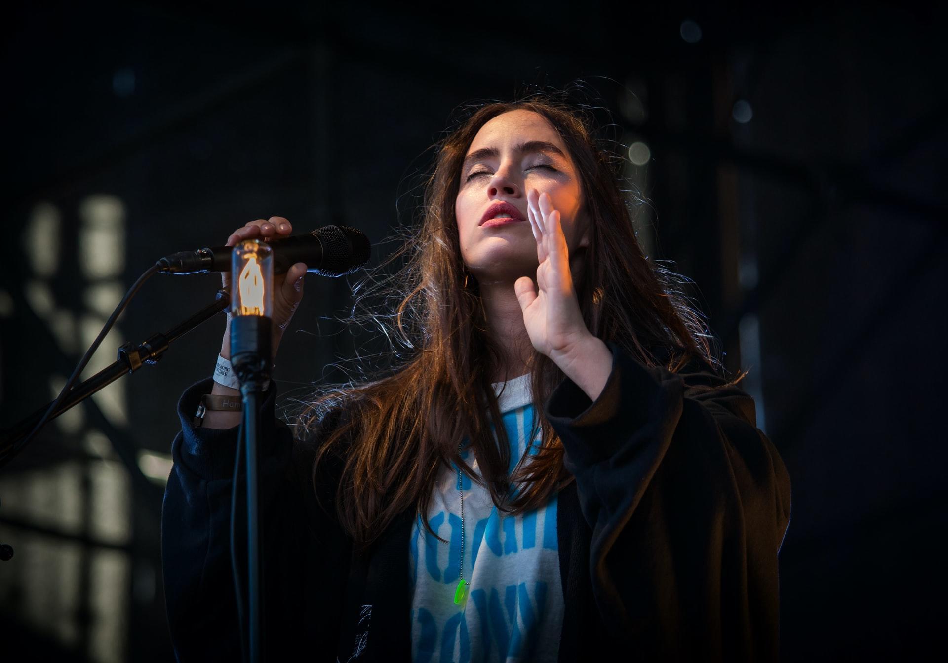 Woman singing by a microphone in a black background.