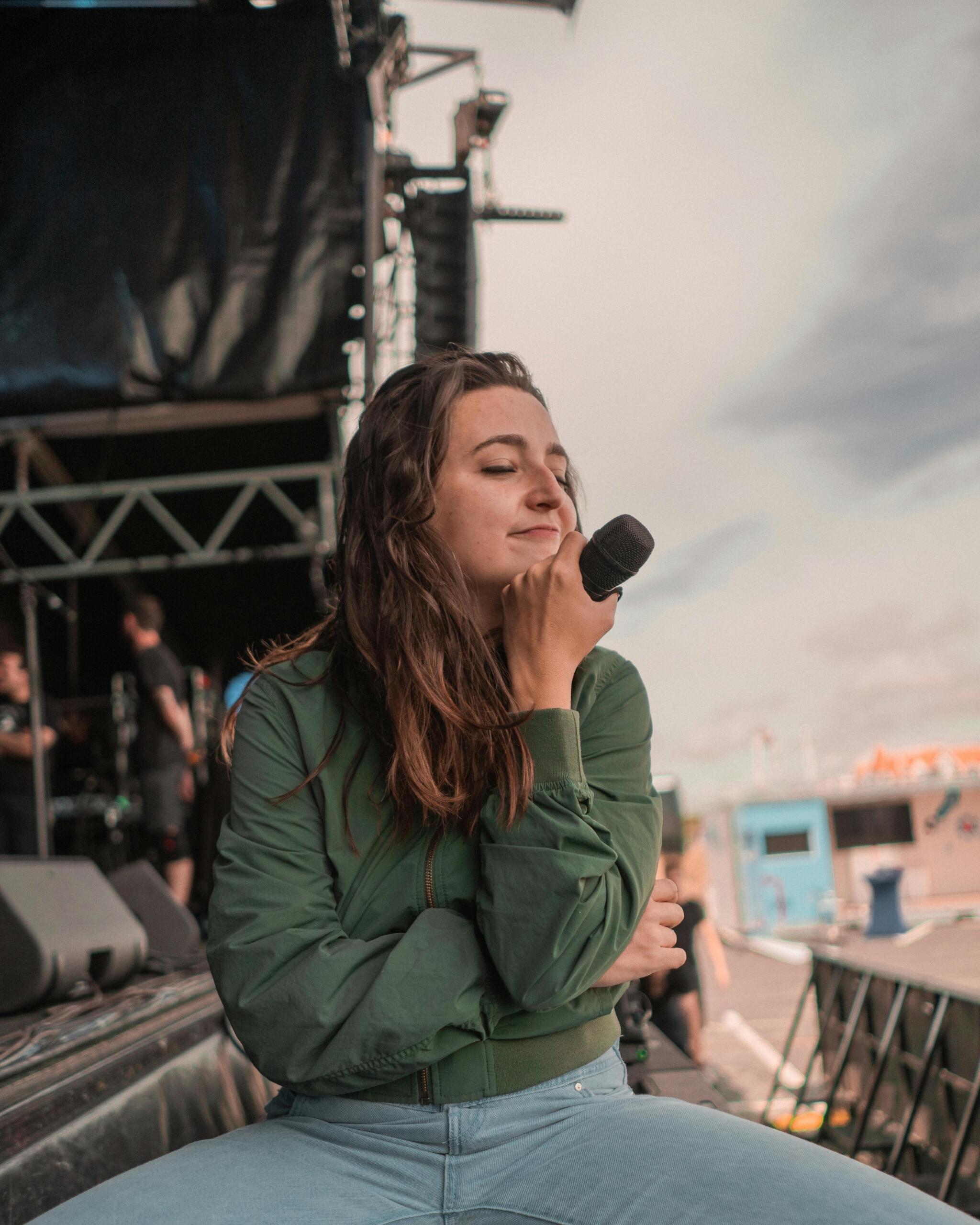 A woman in a green jacket holding a microphone while singing on stage.