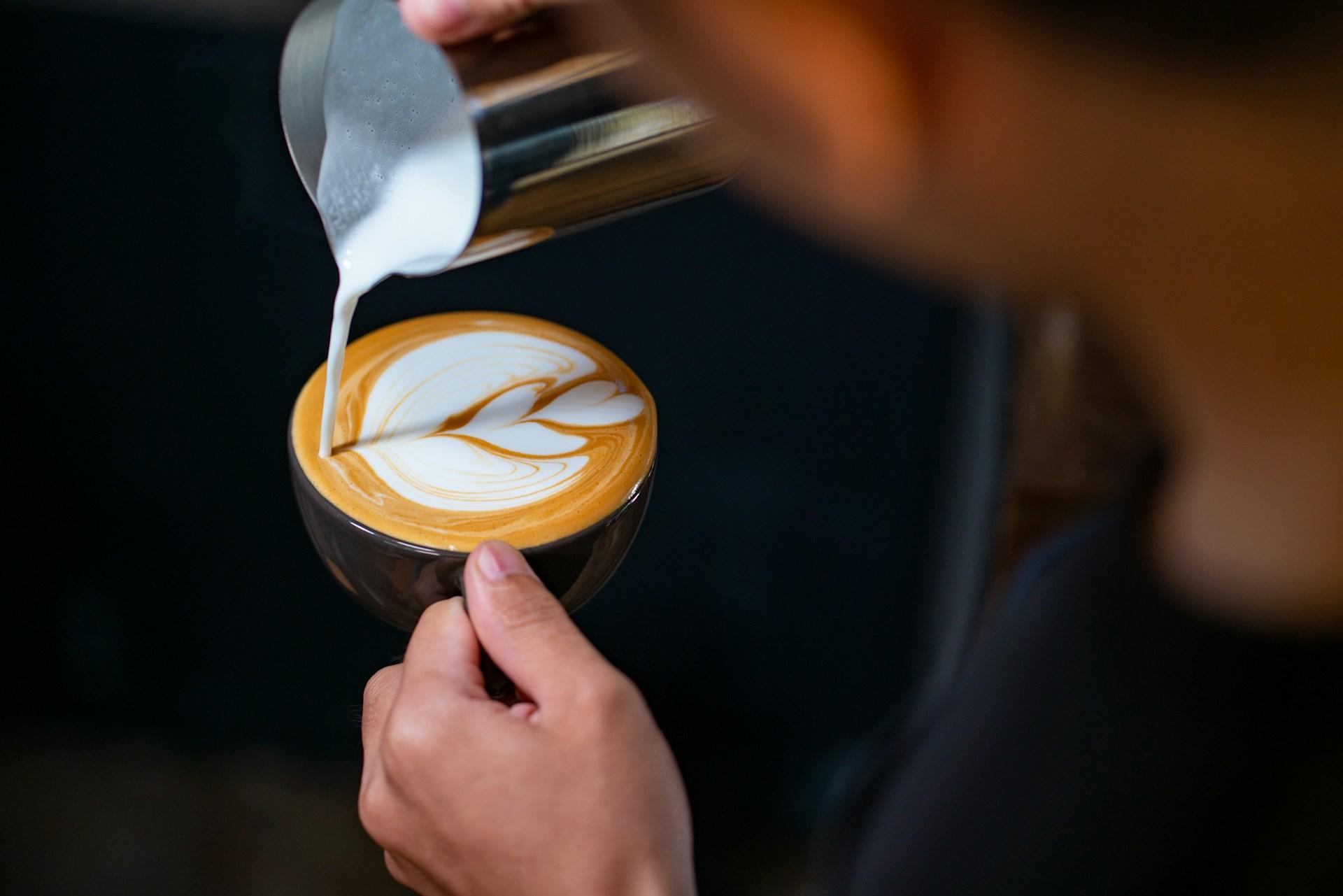 Someone pouring milk to create latte art.