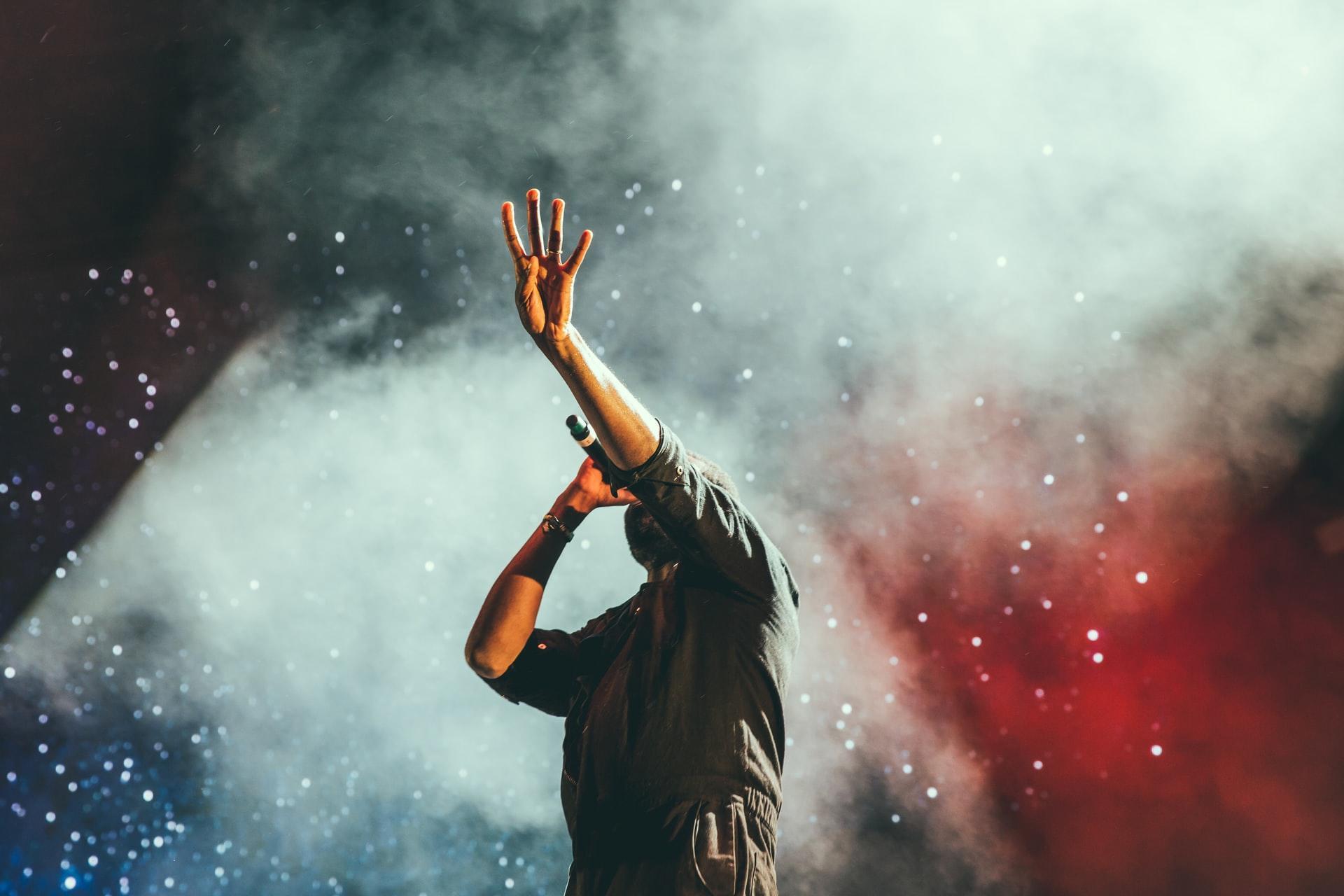 Man singing on stage with hands up in colorful smoke