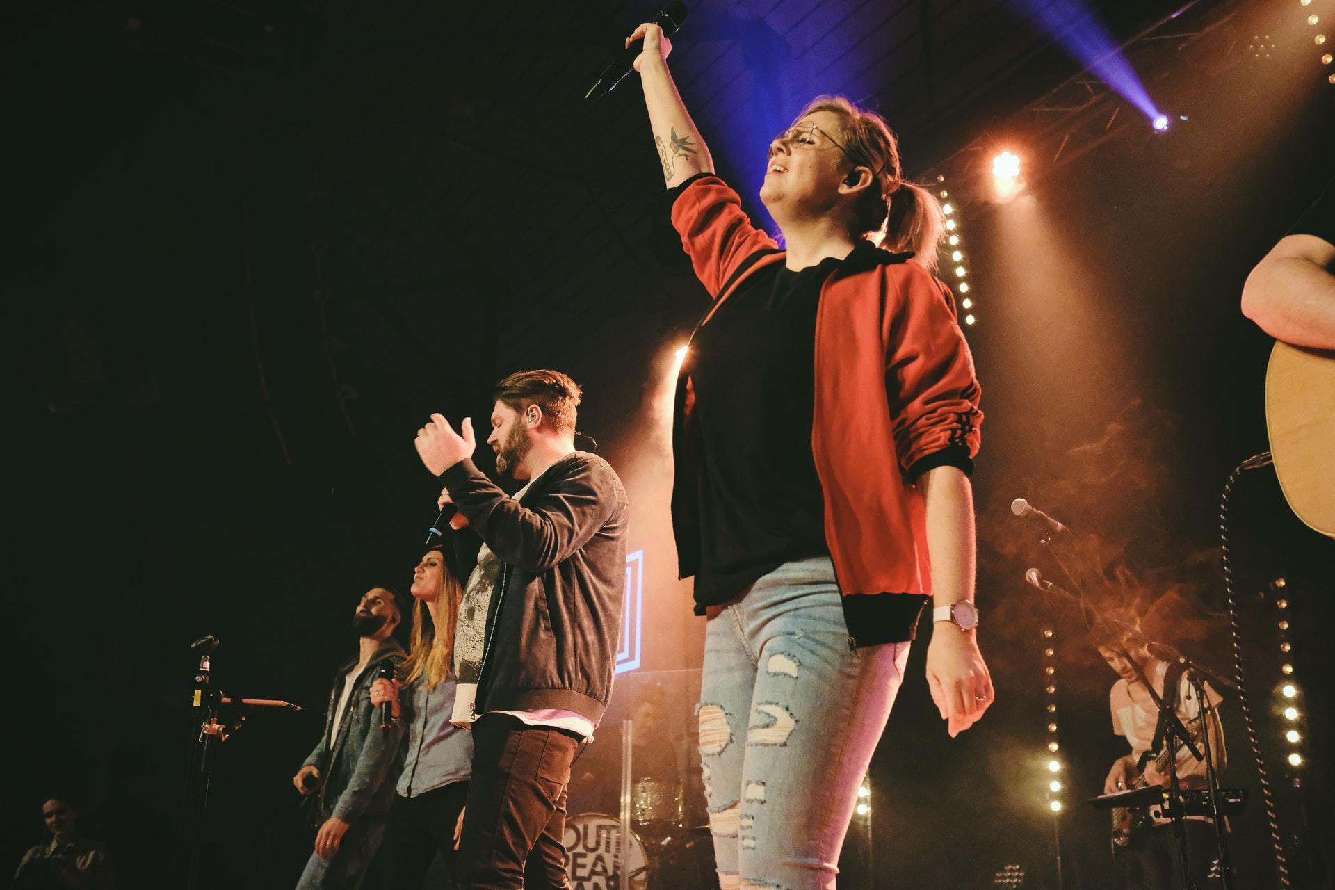 Men and women standing in a line of stage, raising arms to sing.