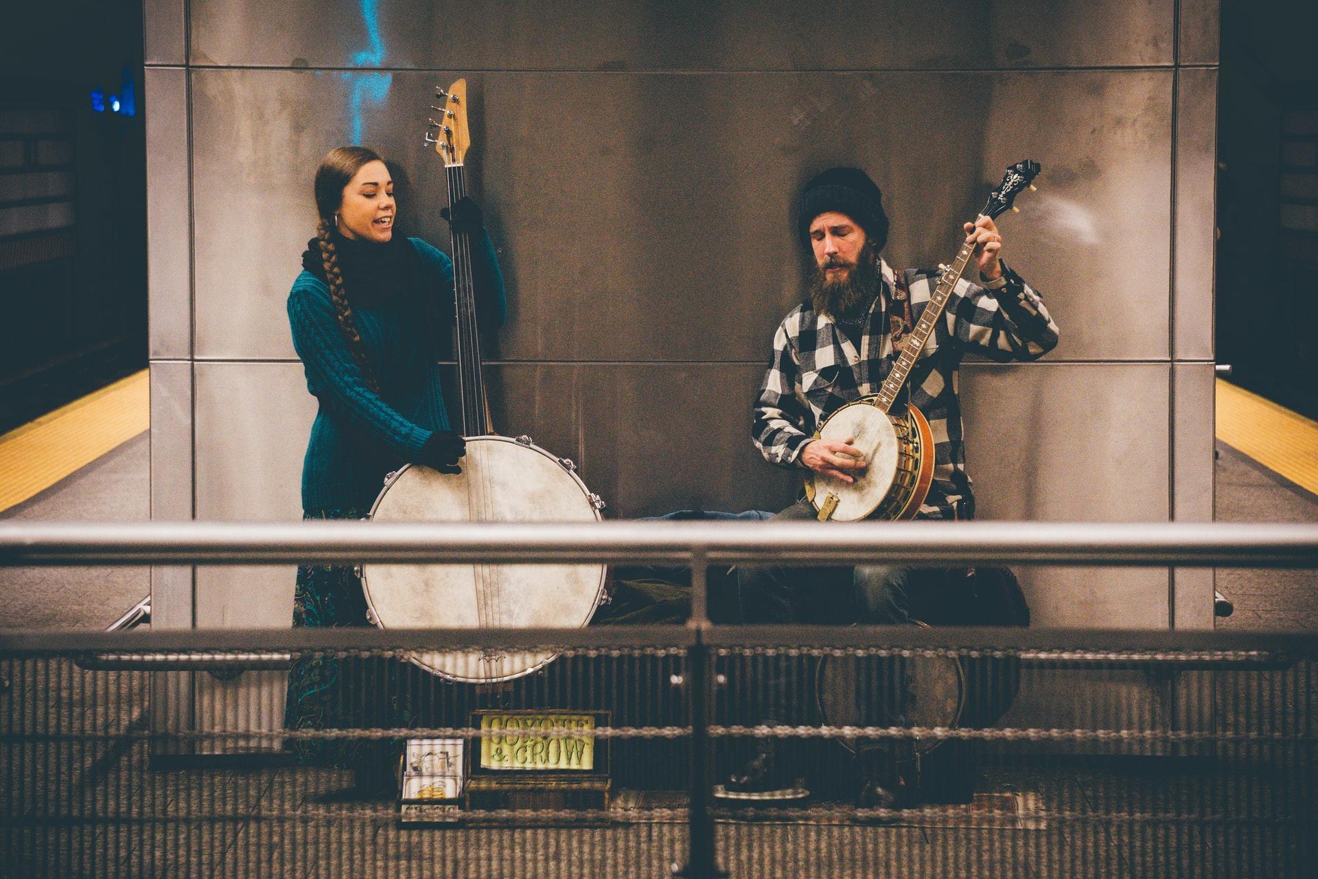 A man and woman playing instruments and singing in the subway.