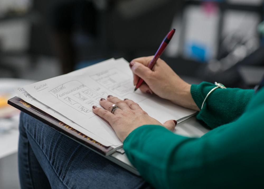 A person holding a paper in their lap and writing on it with a pen. Make sure to go over the ACT English practice tests if you want to reach your target score, and if you wish to be completely prepared, hire a private tutor