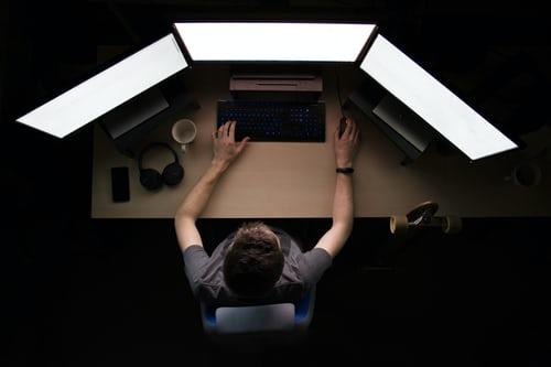 A man facing three monitors while sitting on his desk, because as a computer-programmer-working, you must learn to multi-task. It is usual for coders and programmers to zone out during extended periods of coding; the process is quite taxing