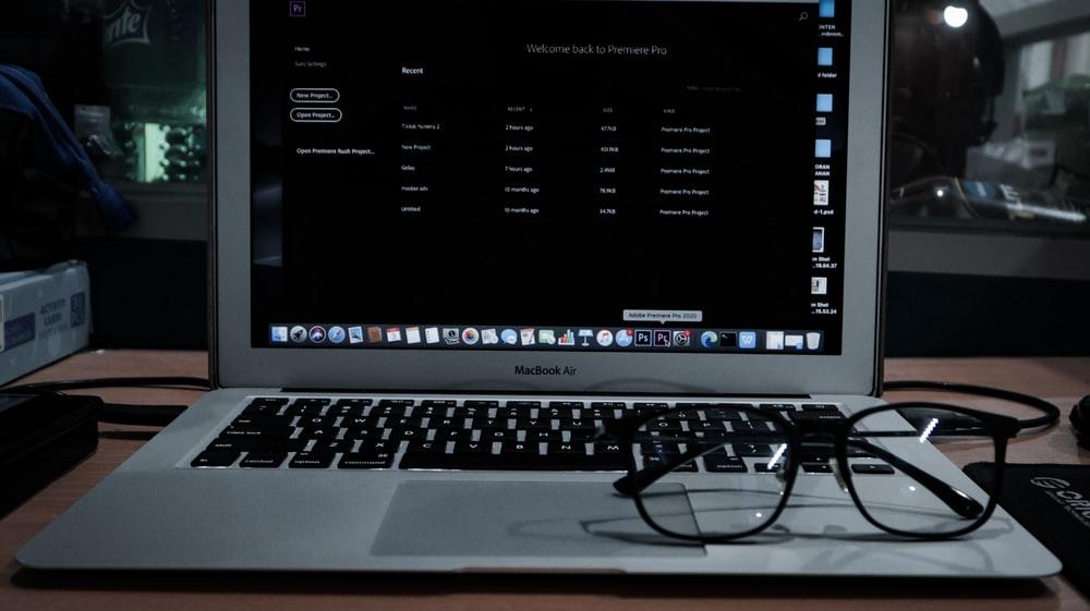 A MacBook Air with glasses resting on it. Adobe After Effects works for desktops and most laptops, and it is faster than other video editing programs; however, some of the features on AAE may be better on other editing platforms