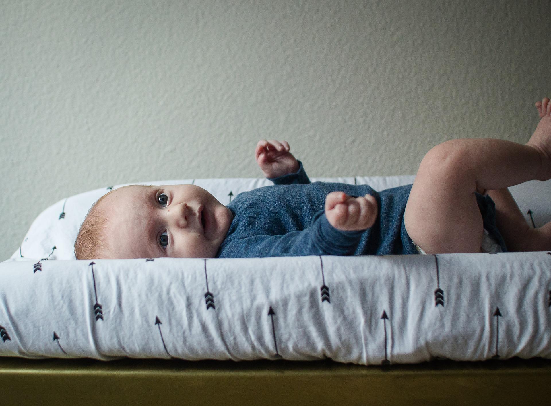 A toddler is lying on the table waiting calmly for the babysitter to change his diaper. If you're new to babysitting and face soiled diapers for the first time, it may help to watch a YouTube tutorial and follow the steps in order!