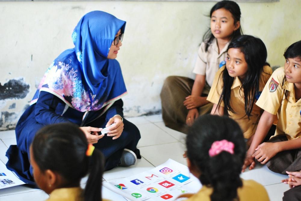 A woman in a blue hijab coaching a group of students in school uniform. Many tutors opt for this profession because they love interacting with young people and want to help them think for themselves