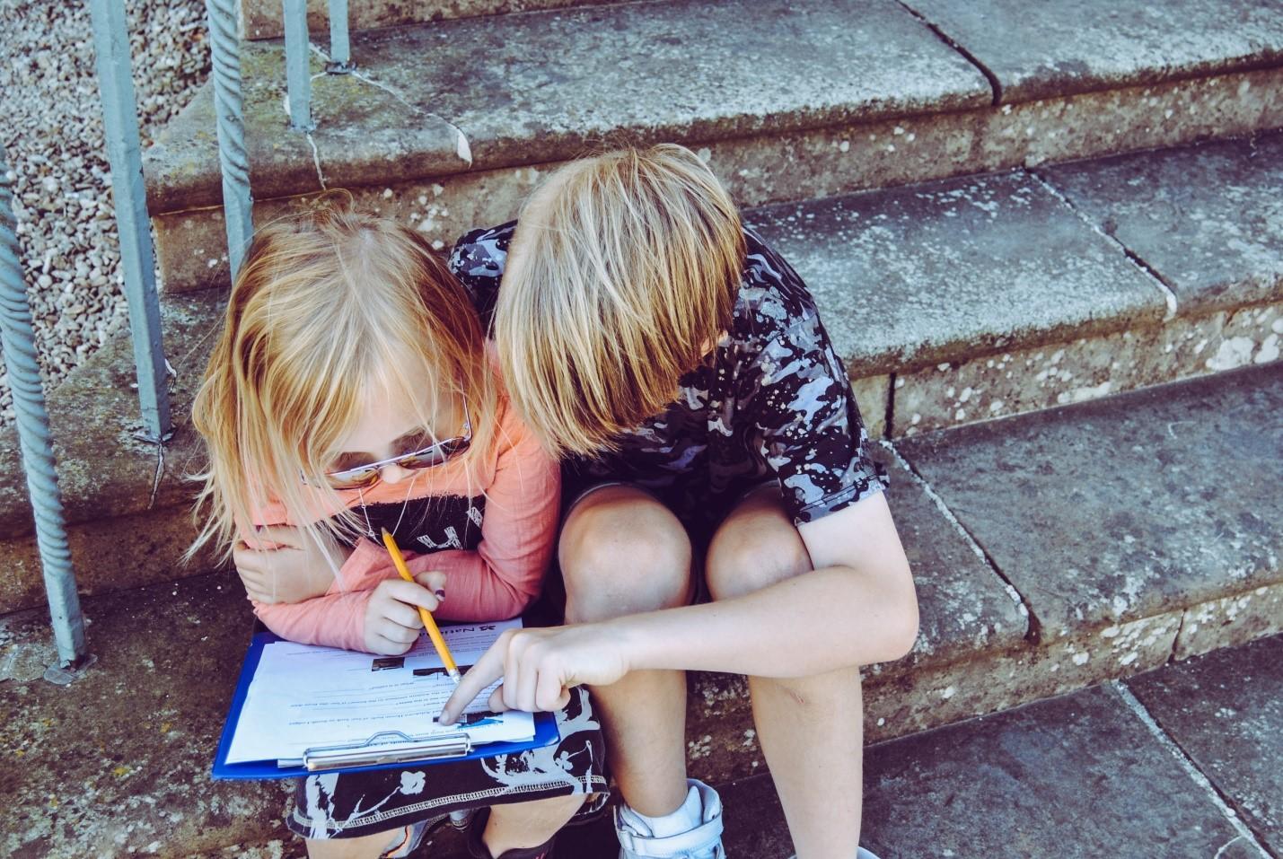 Two kids are seen wracking their brains to finish their homework. Babysitting doesn't essentially include the responsibility of helping children complete their school tasks; however, some babysitters may do it if initially agreed upon