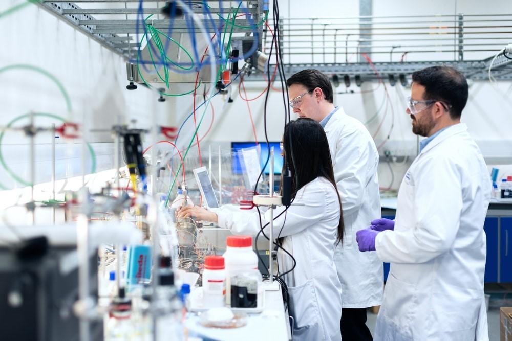 Two men and a woman wearing white lab coats working inside a laboratory with wires, jars, and a computer in the background. Chemistry is a fascinating subject that involves a lot of practical work and experimentation