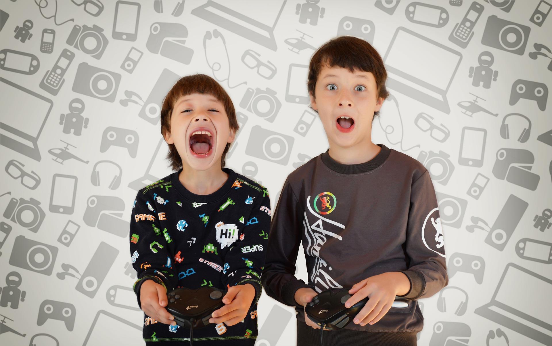 Two kids who are playing video games with different gadgets behind them as the background. Coding games for kids is a great way to encourage your child to become a future computer programmer!