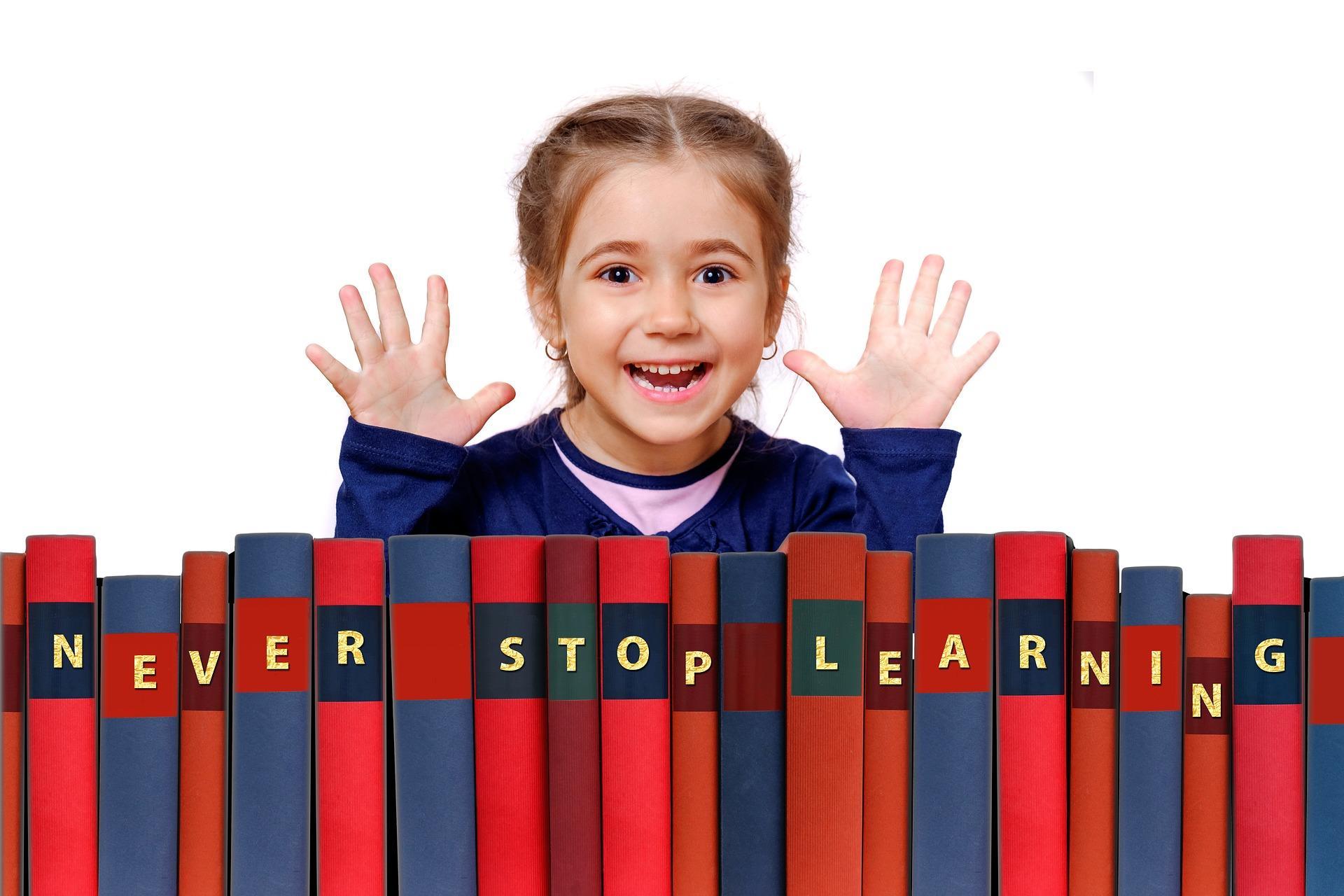 An excited child behind many books lined up to read out ‘Never stop learning.’ There are some great coding programs for kids that can help them get started on this skill early in life