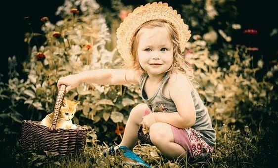 A baby girl sitting in the grass near bushes along with a cat in a basket. These are the best times of a child's life, so ensure they experience positive nurturing. Consider advertising babysitting jobs and find qualified individuals to help you in taking care of your children