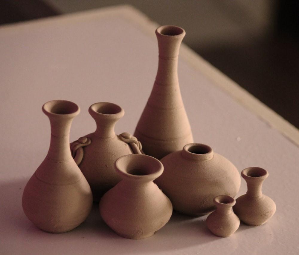 A set of 7 differently sized clay vases resting on a white surface. A pottery wheel allows you to change the length and diameter of your cylindrical pots and vases; however, learning how to use one can be tricky at the beginning