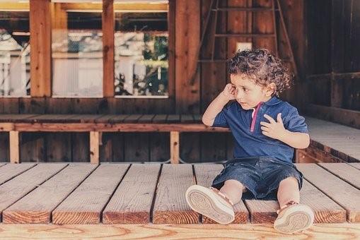 A toddler sitting on a patio pretending to speak over the phone. By hiring a babysitting professional or a nanny, you can rest assured that your child is being cared for while you are away from home handling work or chores