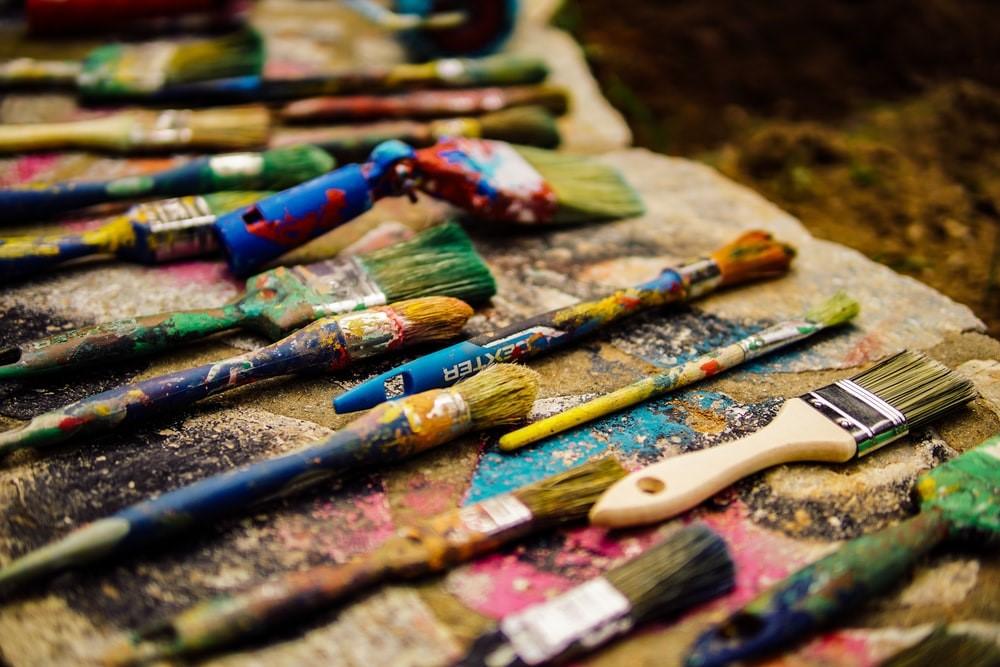 Multiple paintbrushes of different sizes and thickness are spread across neatly on a stone painted some time ago. The brushes are messy and have paint on them; however, some are completely clean. Studying art and committing to it will leave you with a collection of tools similar to this