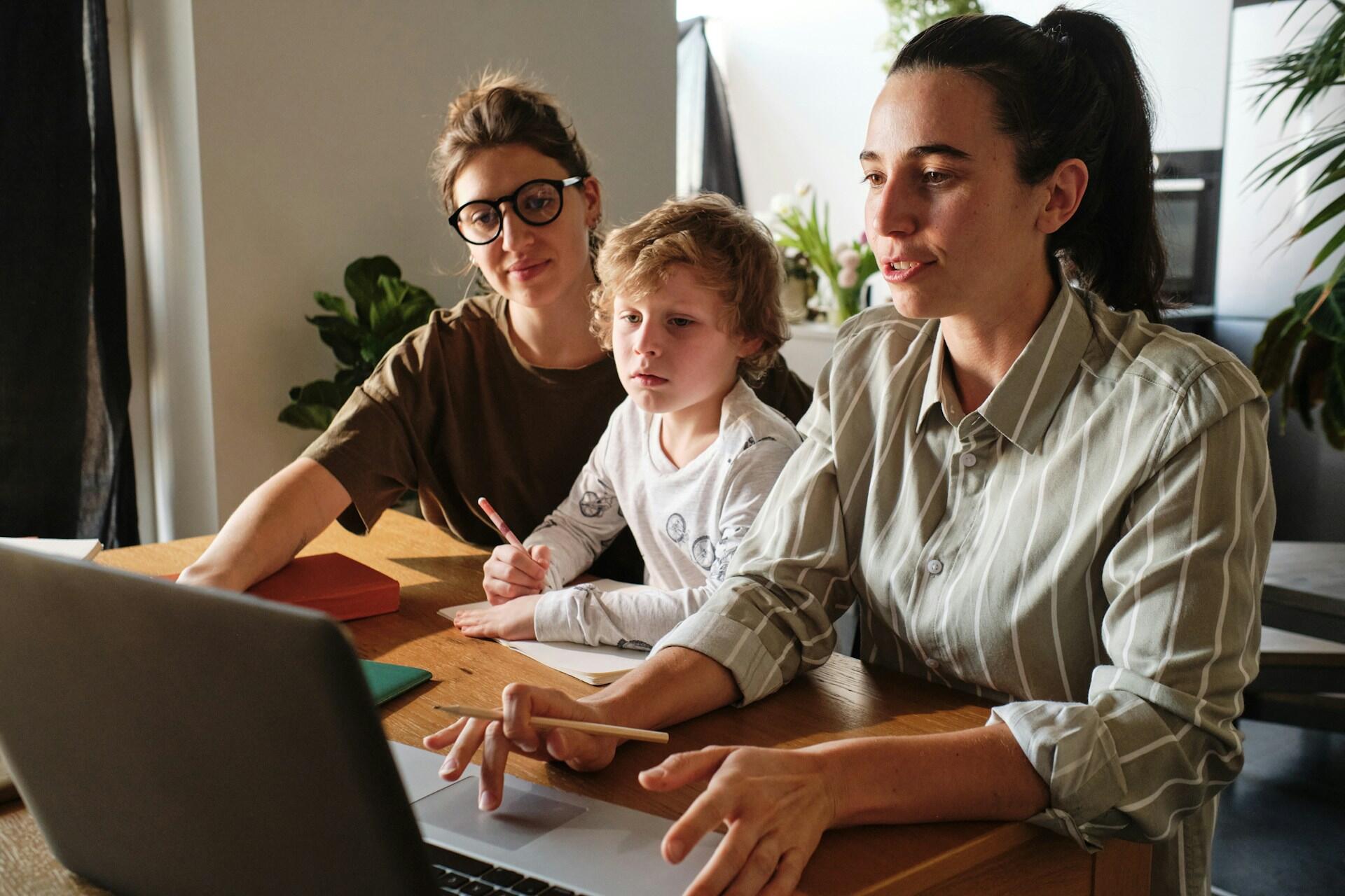 A tutor teaching a child and another lady in front of a computer.
