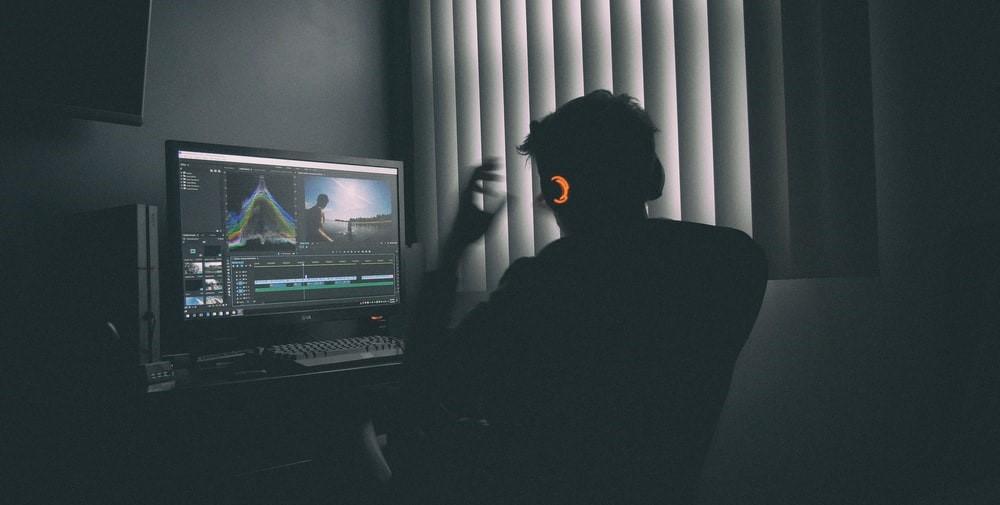 A man listening to music on headphones while staring at a computer screen. Adobe After Effects tutorials can help budding designers with video editing. Sign up with Superprof to learn the basics of the program