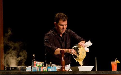 Bobby Flay emptying the contents of a dish into a plate on a chef's counter with cooking ingredients laying on the side. Being one of the top chefs in America, Bobby is well aware of the right amount of ingredients to be used