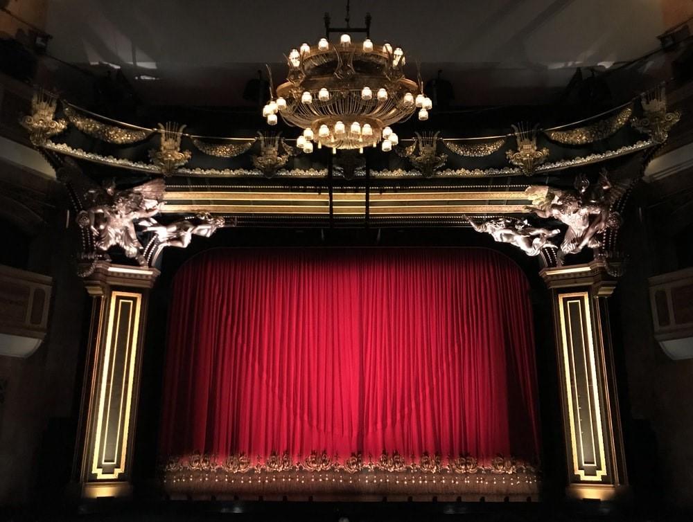 A theatre stage with the red curtains pulled as seen from the audience's viewpoint. Broadway sets are elaborate, exquisite, and rival many modern movie sets you can find in Hollywood