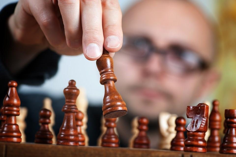 A chess player is moving a pawn to the right place. While playing chess, take very cautious moves, keeping in mind all the theories you may have learned during your research on chess history. Be sure to move the right pieces at the right moment – nor before – nor after