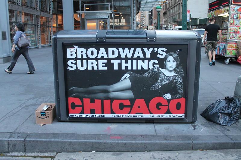 A poster of the musical Chicago with one of the main leads lying across the title and 'Broadway's Sure Thing' written above her. All the posters on Broadway NYC for Chicago the musical are in colors black, white and red