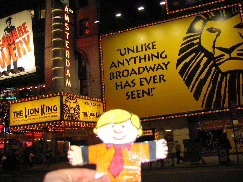 A man outside the New Amsterdam Theater, with promotional posters of The Lion King all over the building. The Lion King was first introduced as a New York Broadway musical in the New Amsterdam theater, after which it started showing at the Minskoff Theatre