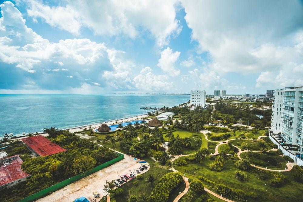 A shot of a beach resort with manicured gardens, a white building, and the sea in the distance. Mexico's coastal cities, like Cancun and Acapulco, are noted for their tropical beaches and make for excellent backdrops to Mexican movies