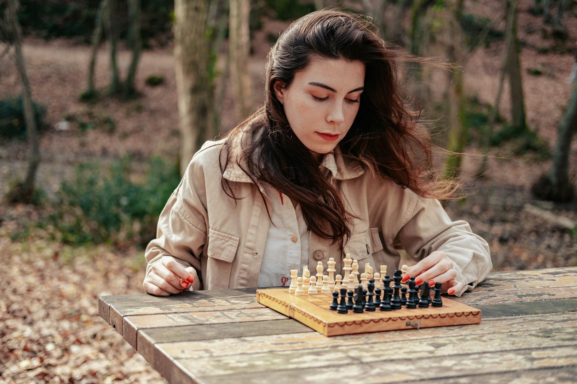 A women playing chess in a park.