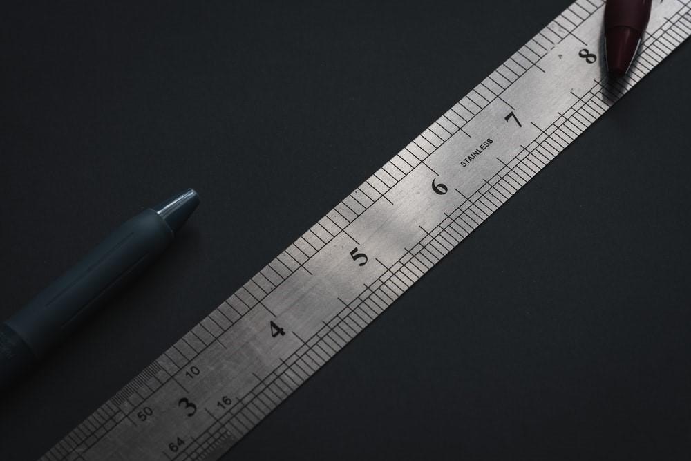 A grey steel ruler and a pen lying on a black surface