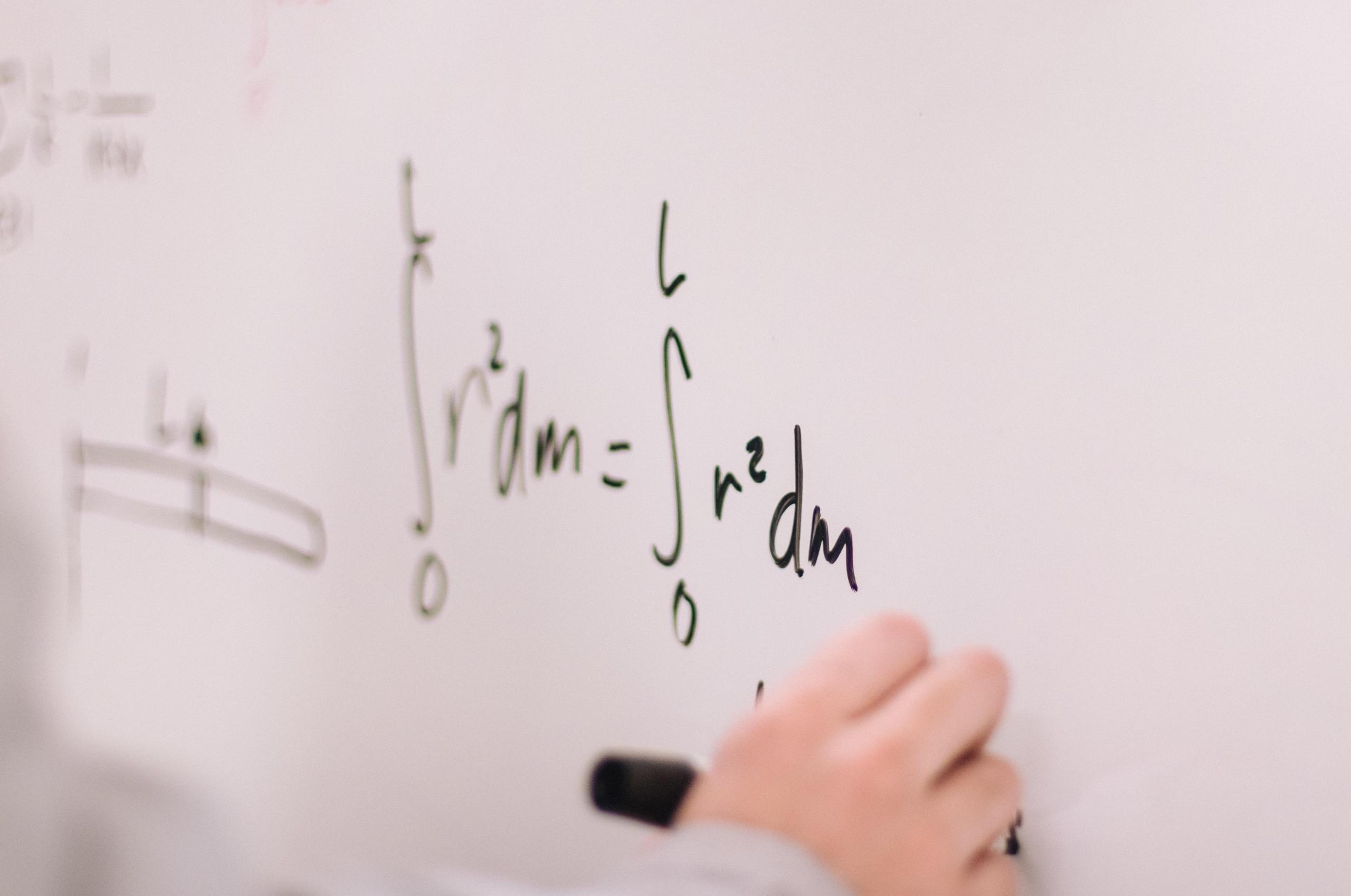 A person writing calculus bases and equation with a black whiteboard marker