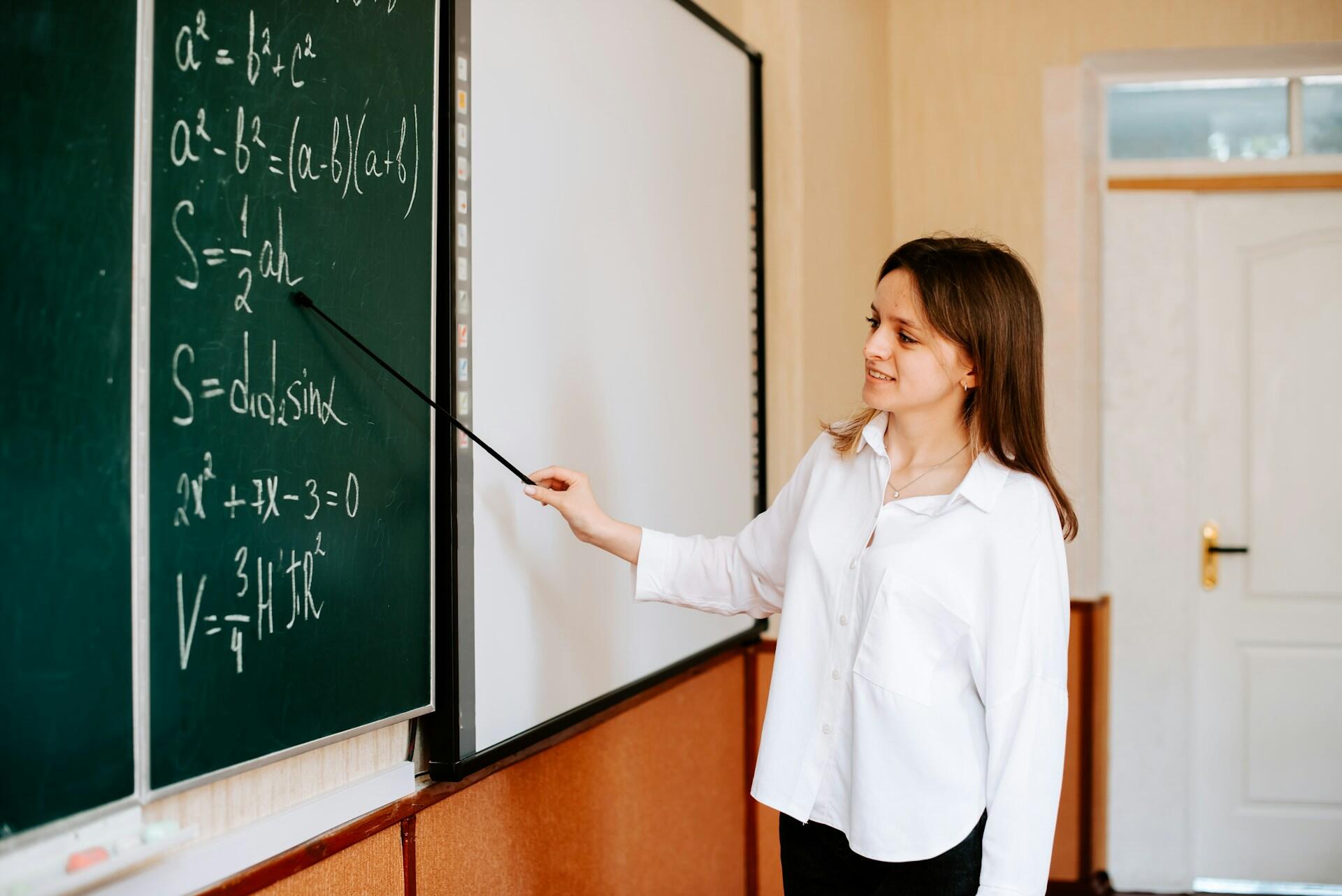 A student in a white shirt pointing at a chalkboard.