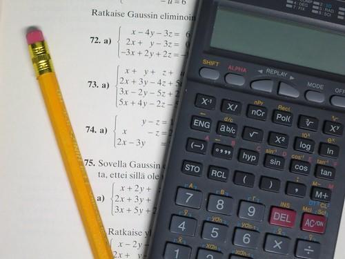 A calculator and a pencil are lying on a sheet with algebraic equations printed on it