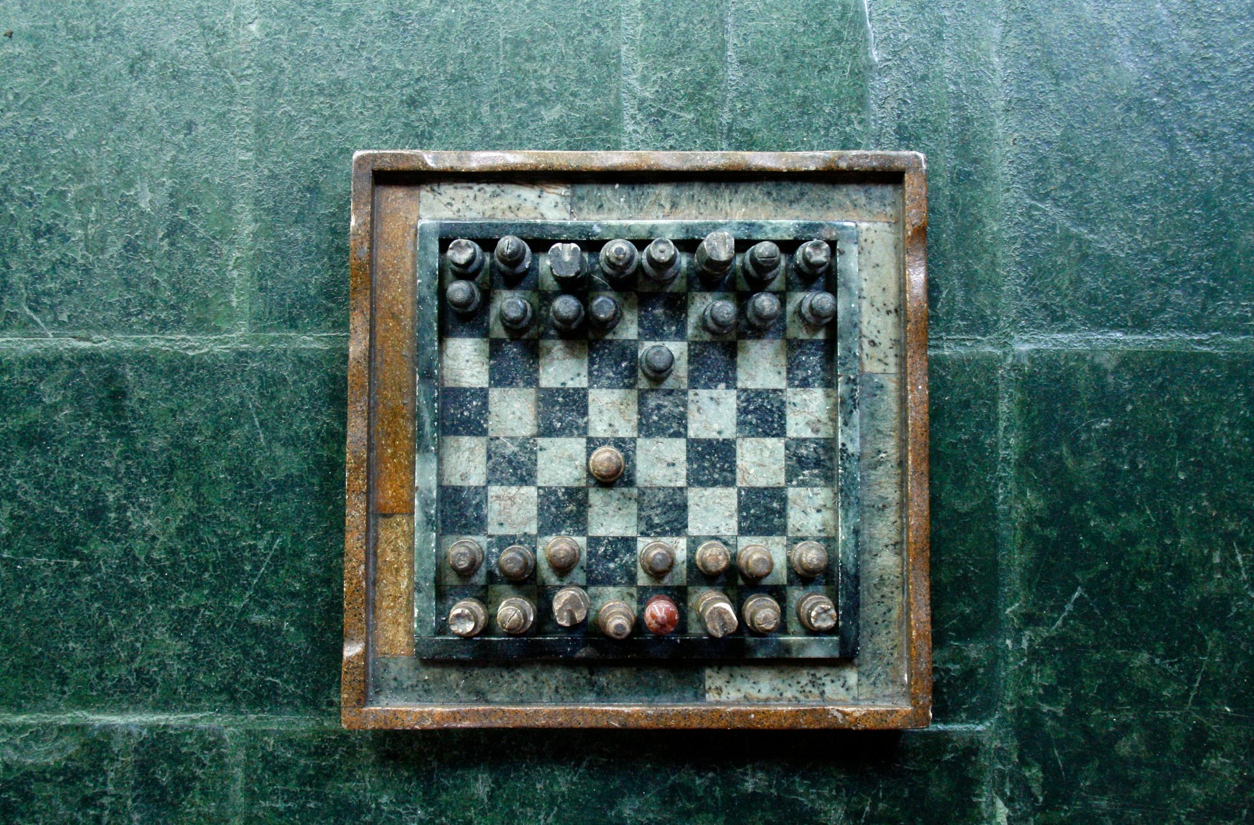 A vintage chessboard is placed on green tiles as the players are about to begin the game. 