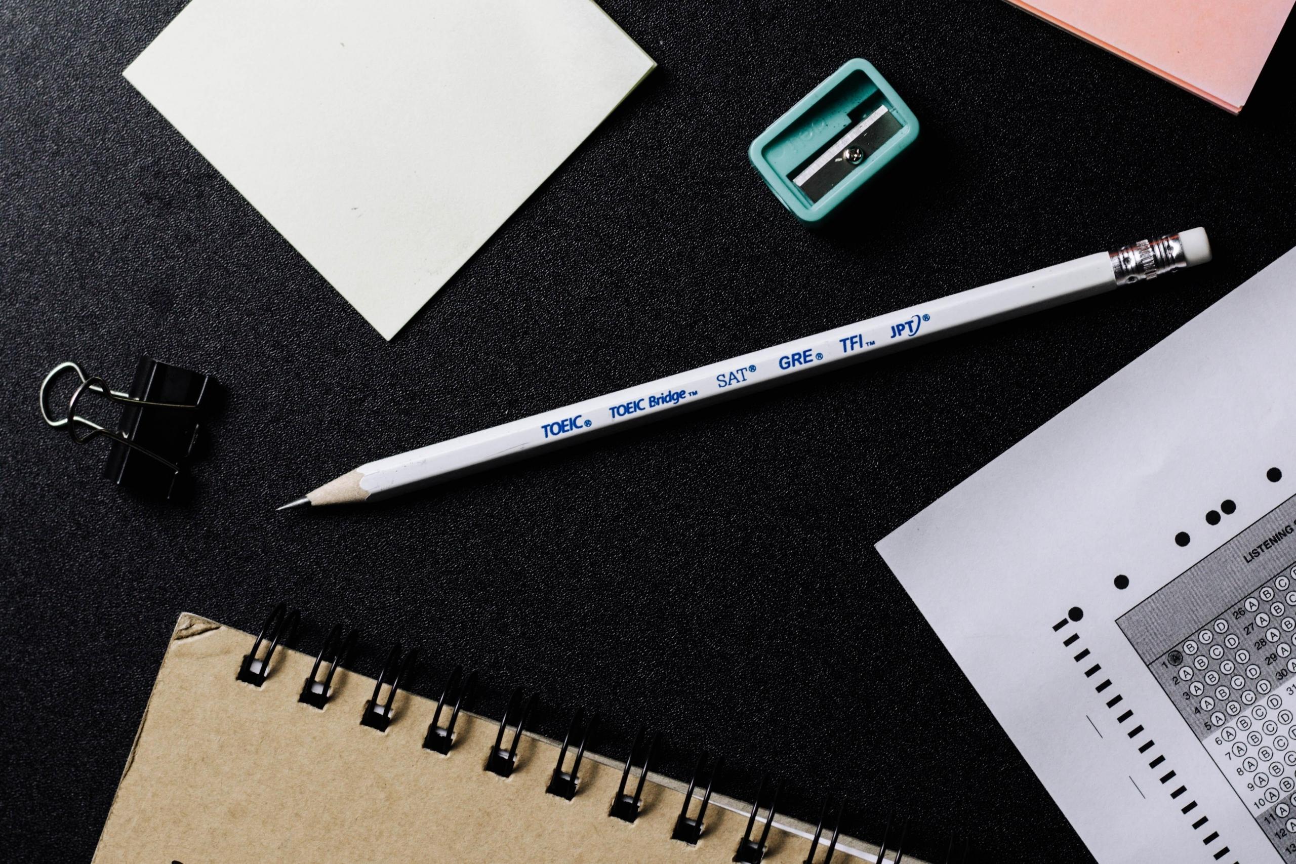 A pencil, sharpener, sticky note, page holder pin, notebook, and a mock AP Chemistry practice test paper is placed on the table