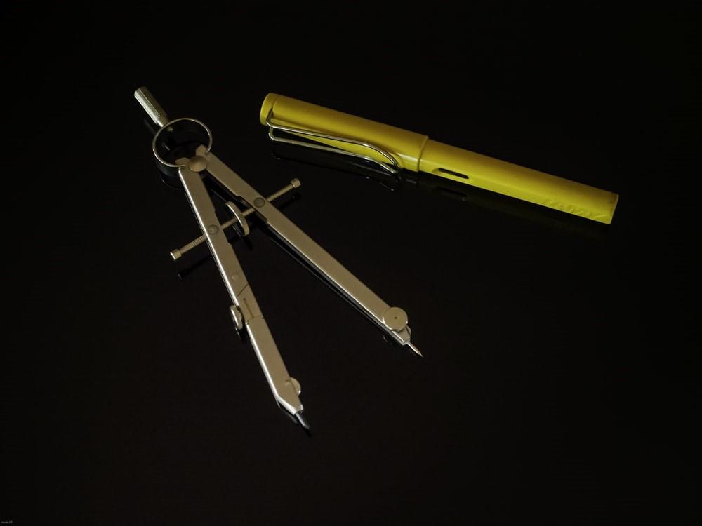 A compass and a yellow pen on a black surface
