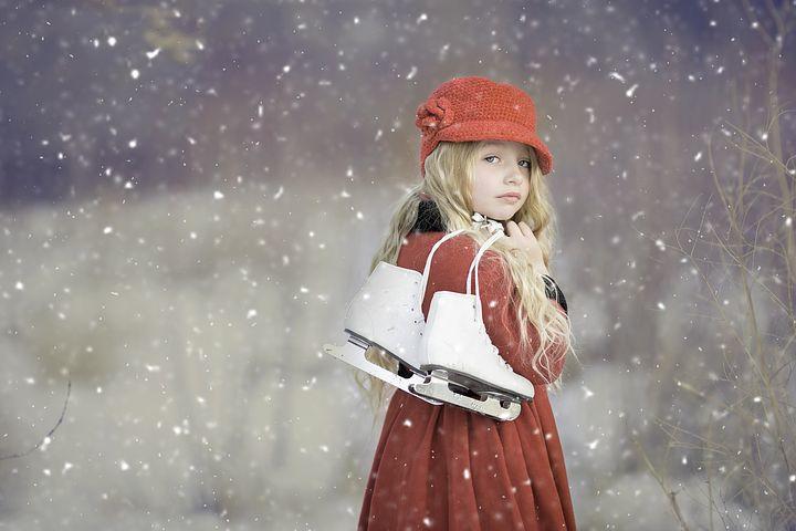 A young girl holding a set of inline skates while snow falls around her