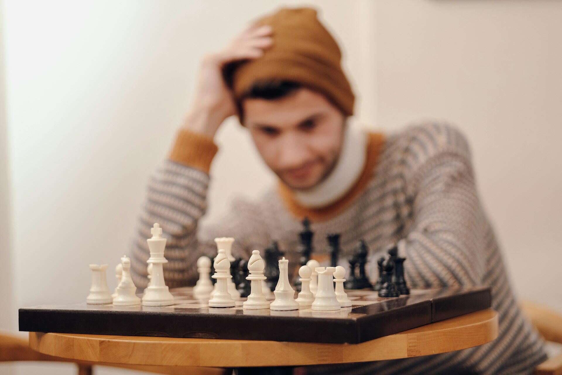 A guy in a mustard color beanie thinking of his next chess move.