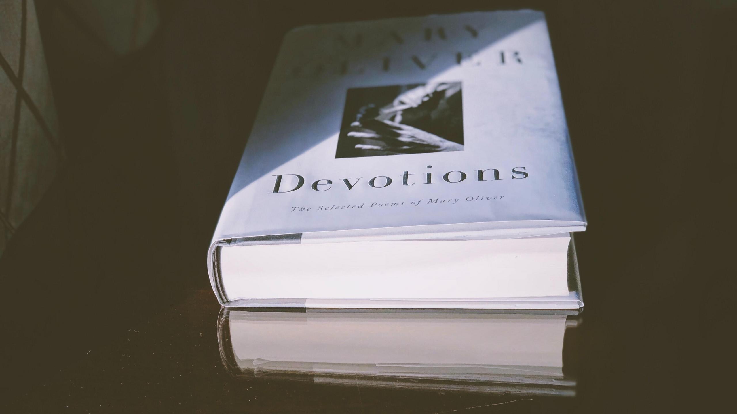 "Devotions: The Selected Poems of Mary Oliver" – a book by Mary Oliver is placed on a table in the dark 