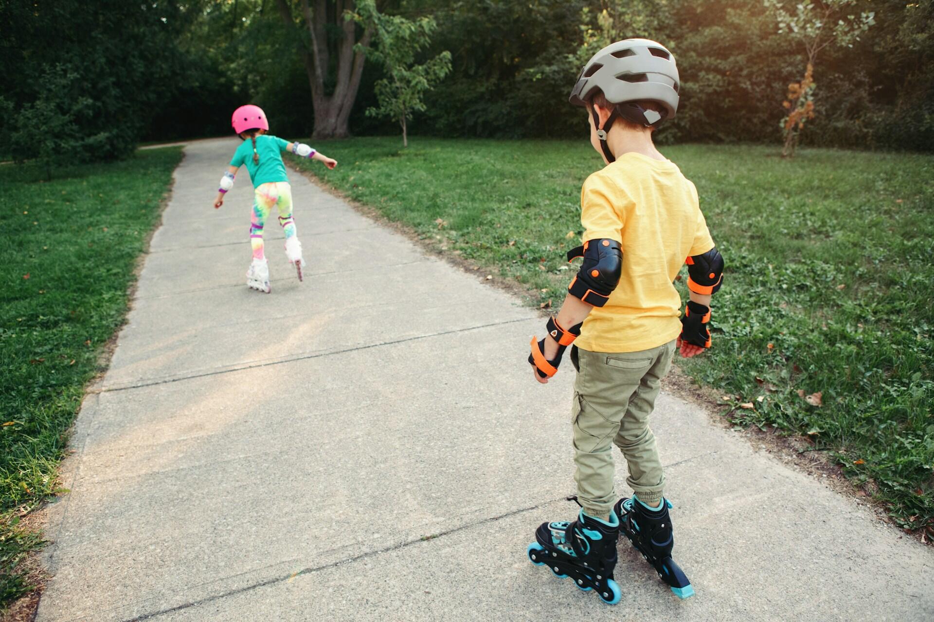 A girl roller skating ahead of a boy and both of them wearing helmets and protection.