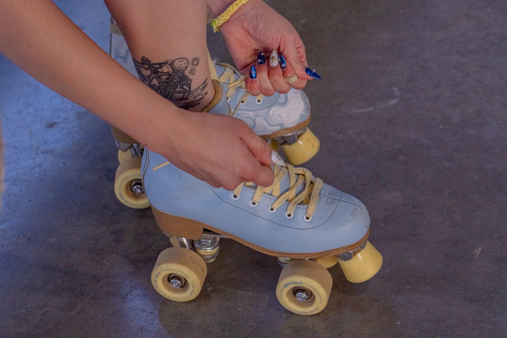 Person tying the laces on a light blue quad roller skate.