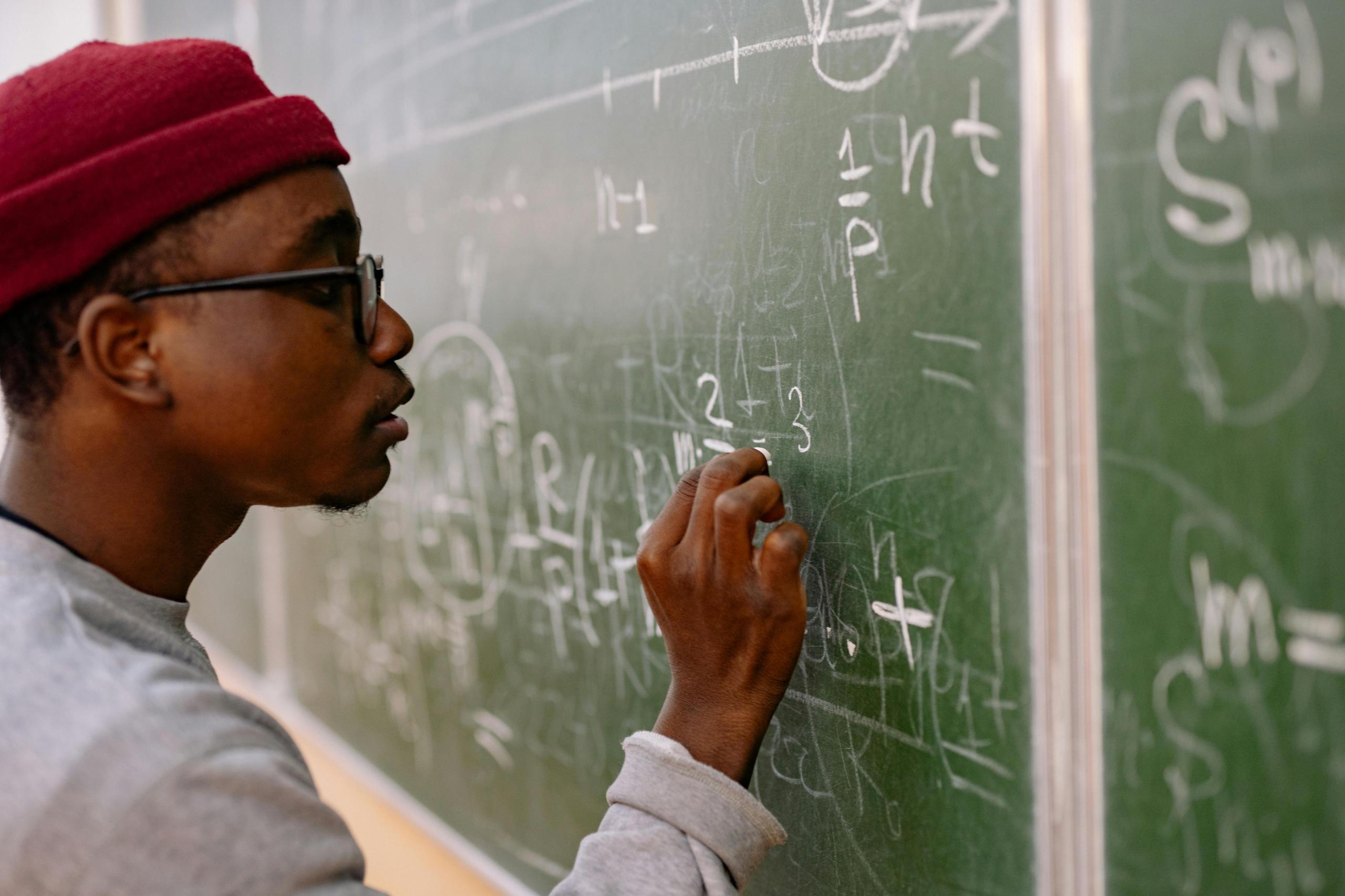 A teacher passionately teaches his students by explaining the formulas that are written on the blackboard.