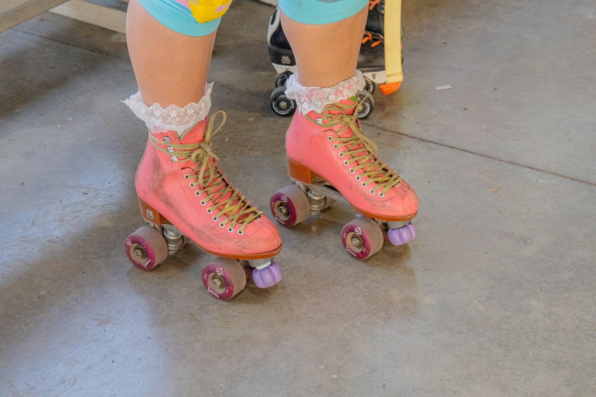 Person wearing pink quad roller skates on a concrete floor