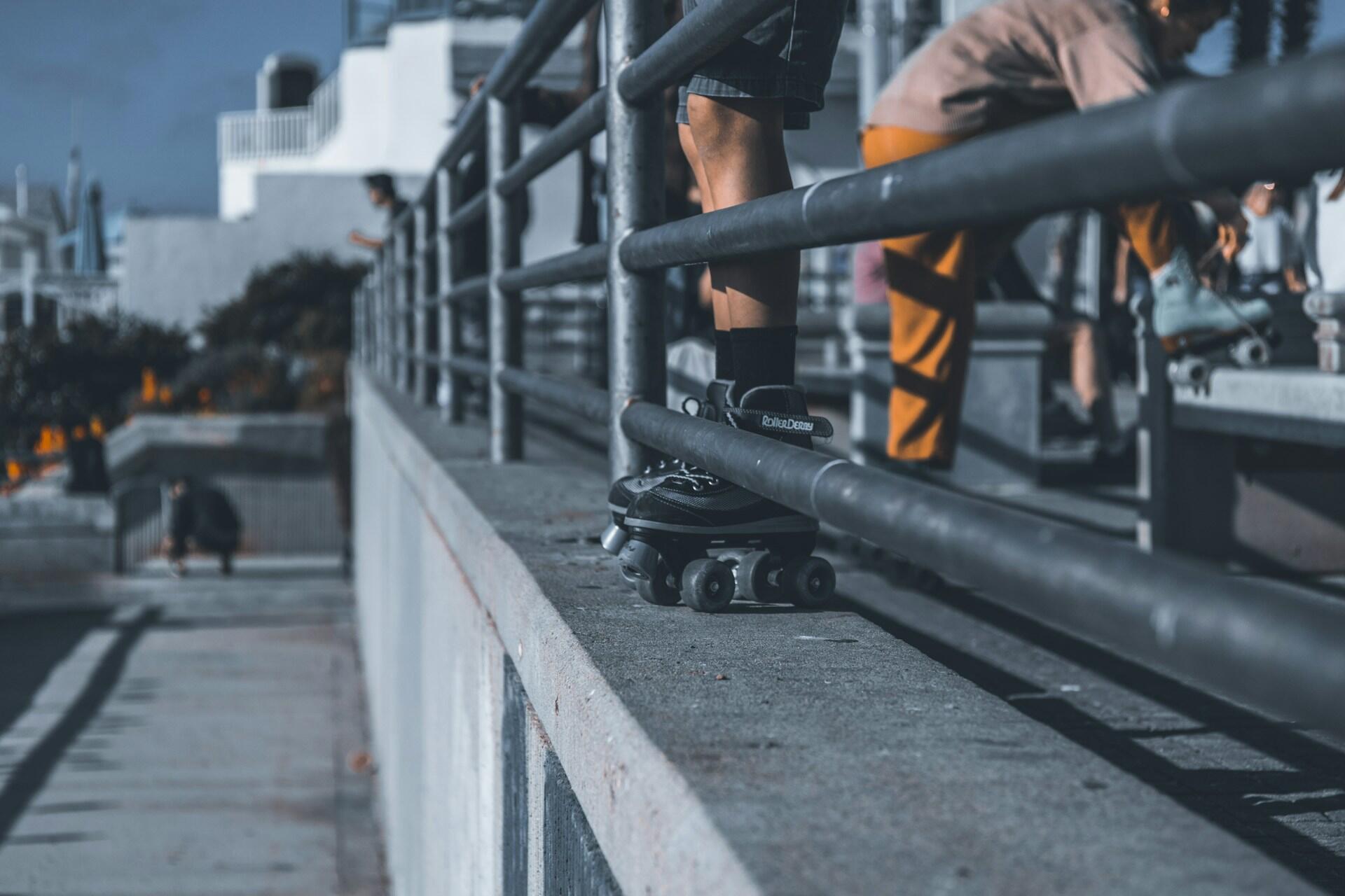 People with roller skates beside a metal railing in an outdoor urban area