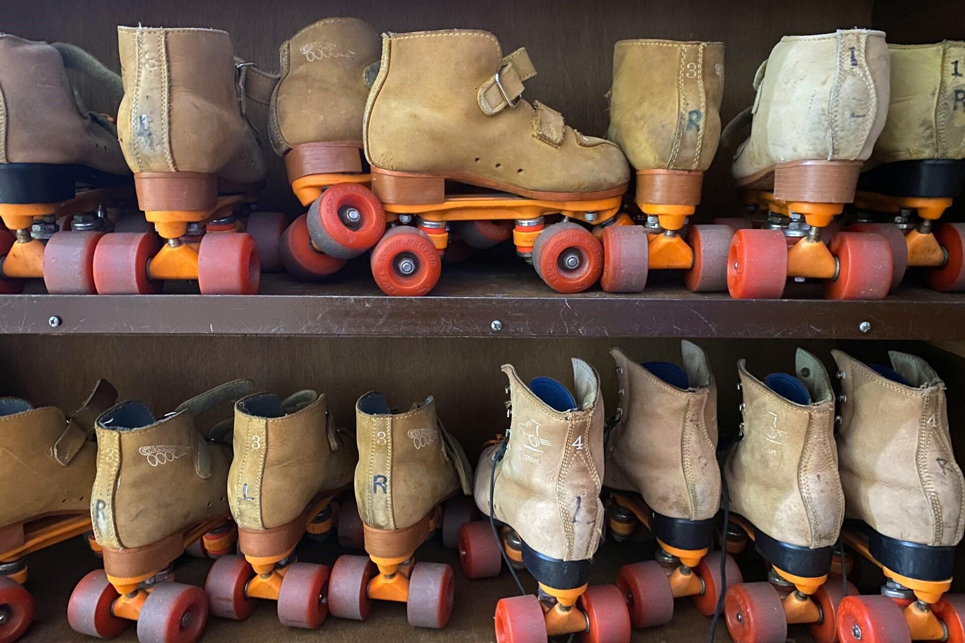 Rows of tan roller skates with orange and red wheels on wooden shelves