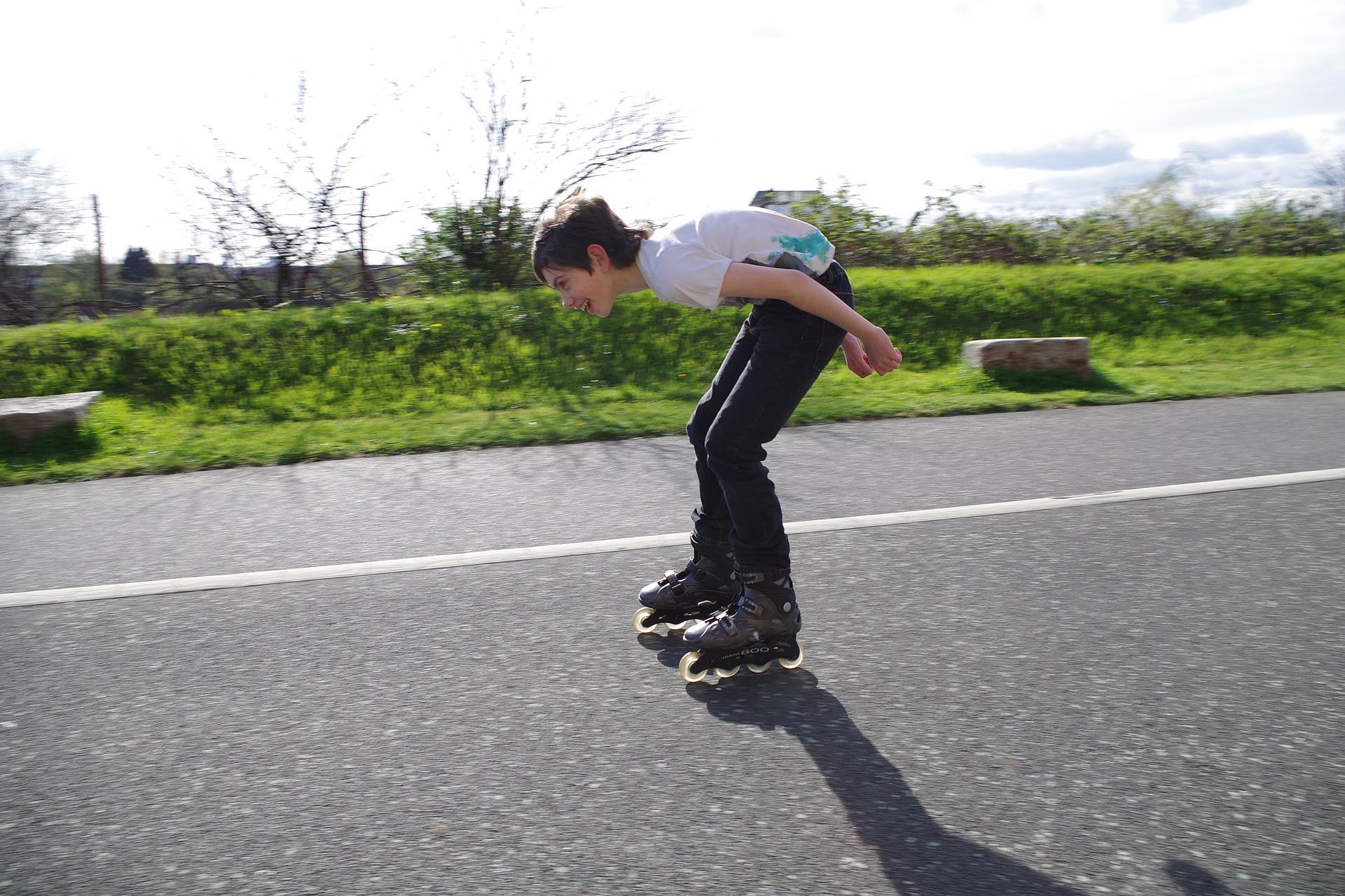 A kid happily and confidently roller skating on a downward road